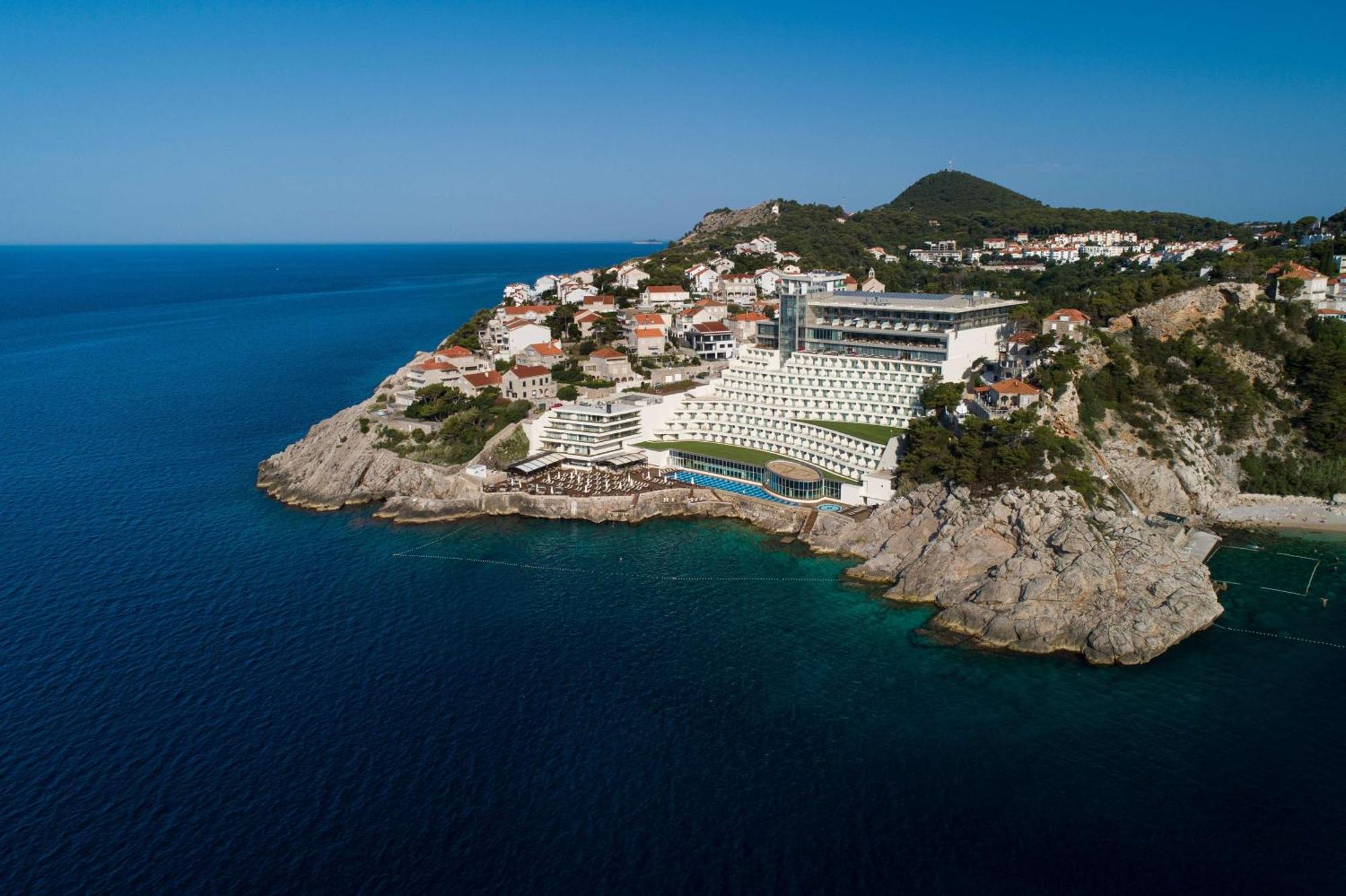 Rixos Premium Dubrovnik Hotel Bagian luar foto The photo shows a stunning coastal landscape featuring a modern hotel or resort situated on a rocky outcrop. The building is designed with a contemporary aesthetic, overlooking the deep blue sea. In the background, there are several residential struc